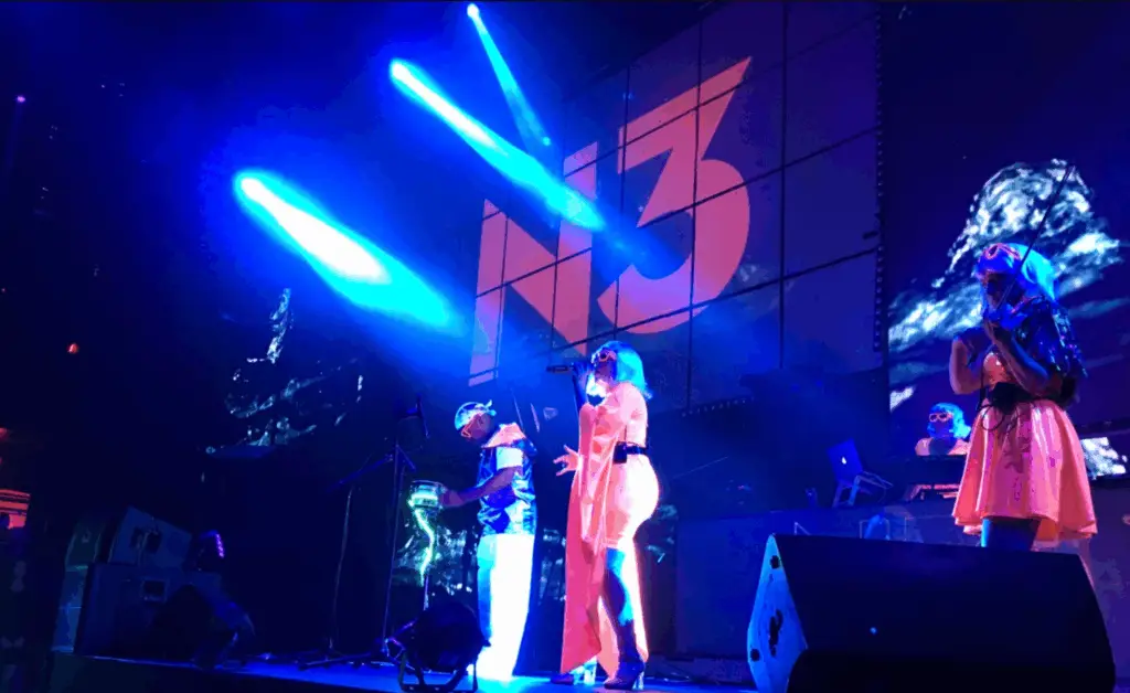 DeeJay Shelly wearing glow wings performing the Glow Show at Mandalay Bay Las Vegas with vocalist, bongo player, and electric violinist in reflective glow costumes – female DJ and live show entertainment